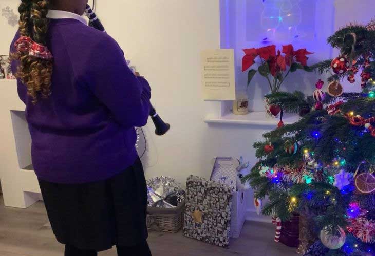 Child playing clarinet in front of christmas tree