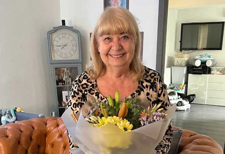 Foster carer, Sue, sitting on sofa, smiling, and holding bouquet of flowers