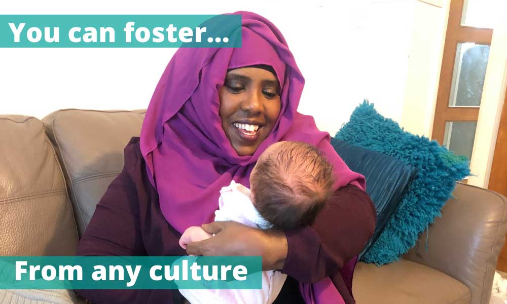 Woman smiling wearing hijab holding new baby she is fostering