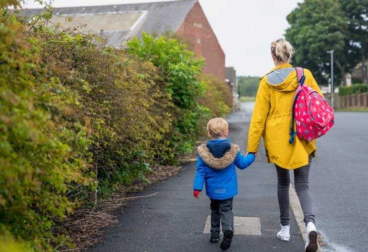 Young boy in school uniform walking hand-in-hand with carer